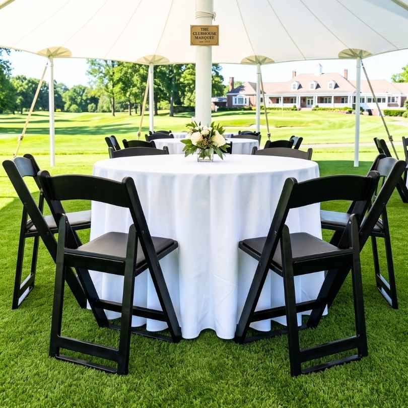 Black chairs around a dining table on a lawn under a tent