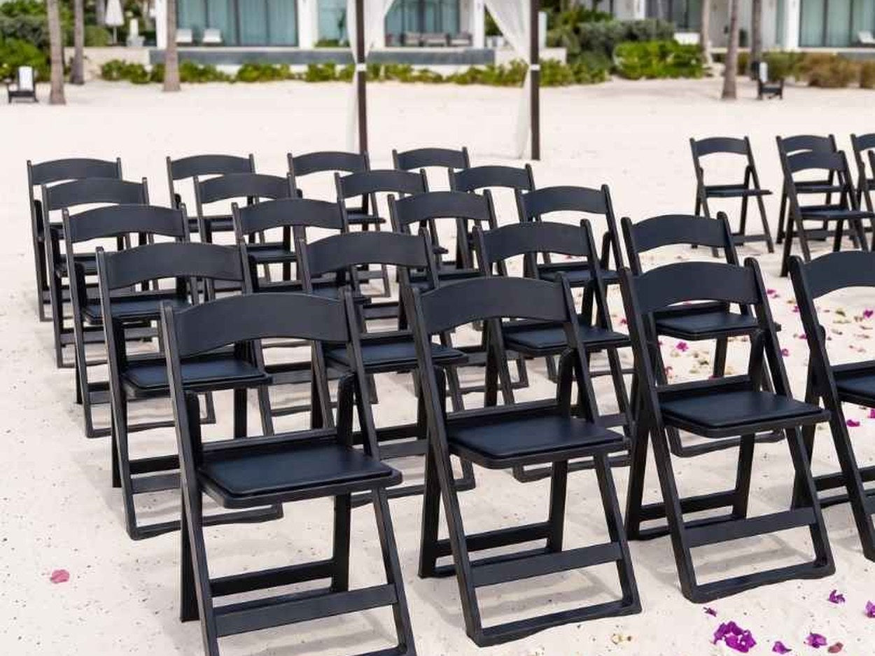 **[Black Grass and Sand Series](https://chivari.com/products/black-grass-and-sand-series-resin-folding-chair-with-black-vinyl-cushion-and-stainless-steel-hardware)** in ceremony rows. The wide feet spread the load so the front legs don't sink while a guest leans forward — the failure that produces the tip.