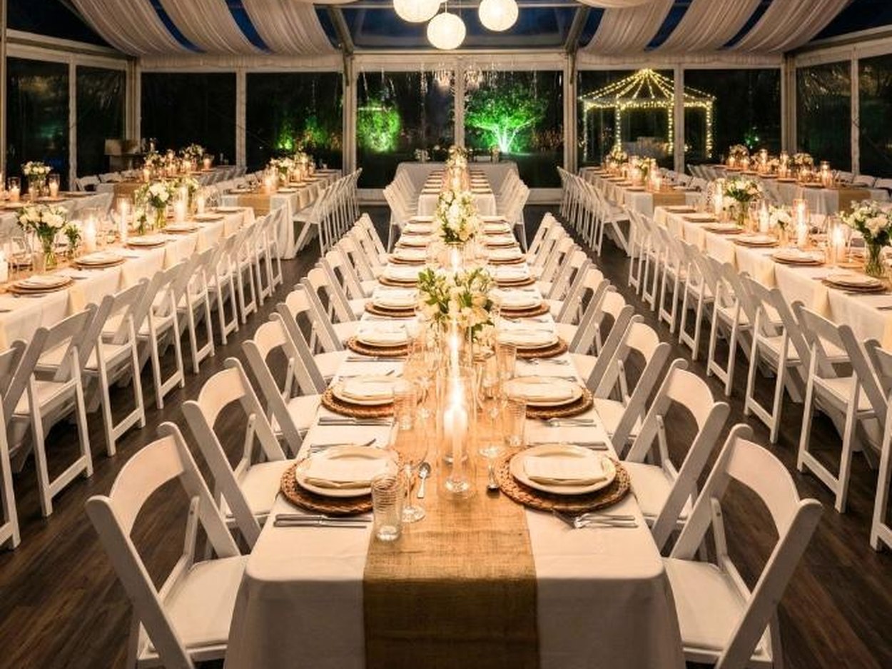 **[Standard Resin folding](https://chivari.com/products/resin-white-folding-chair)** at long tables in a draped room under warm uplighting. Twelve pounds, 500 lbs rated, lowest cost per seat in the resin line.