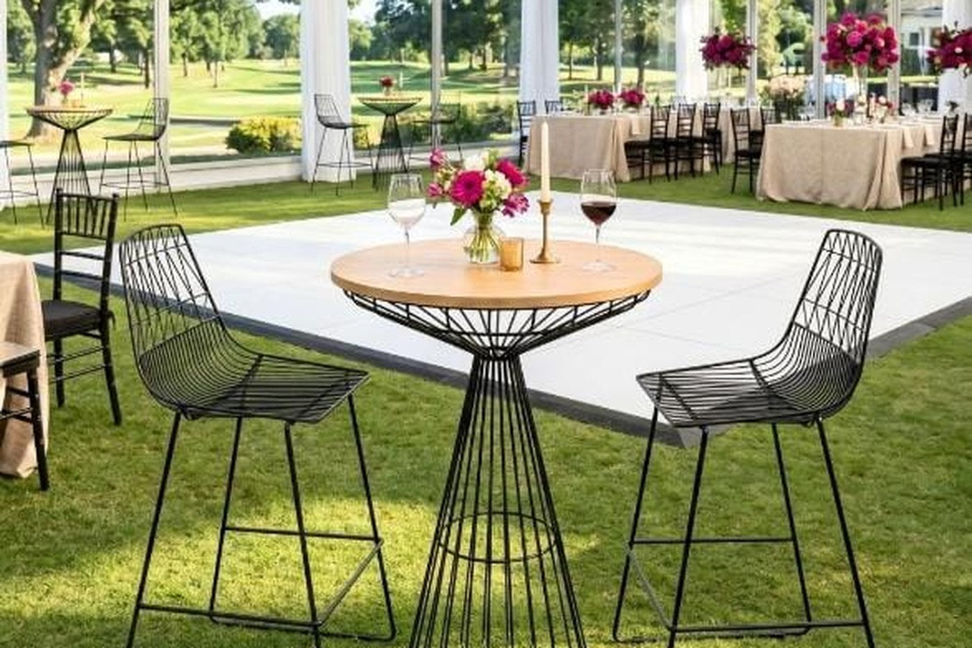 Portable dance floor laid outdoors under a tent with a cocktail table on it