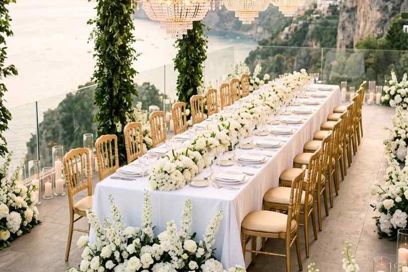 Long banquet table under greenery and florals, set with gold Napoleon chairs